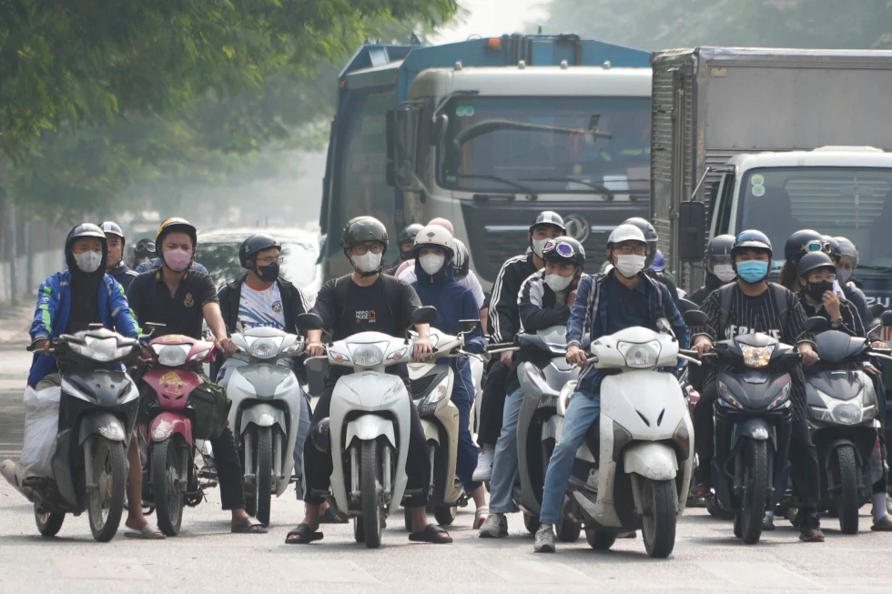 People wearing face masks wait at a traffic signal in Hanoi